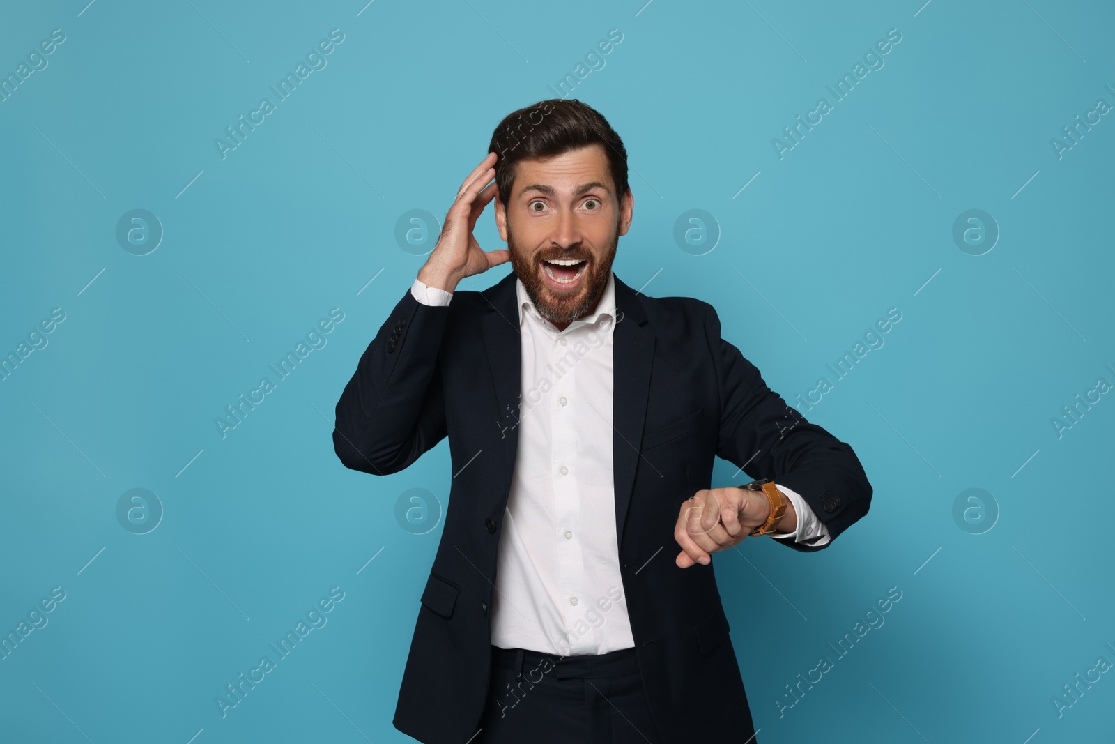 Photo of Emotional man checking time on light blue background. Being late concept