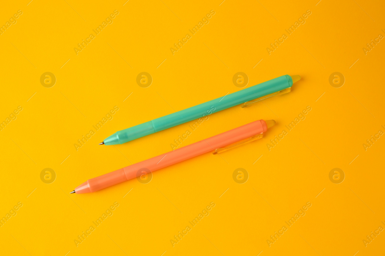 Photo of Two erasable pens on yellow background, flat lay