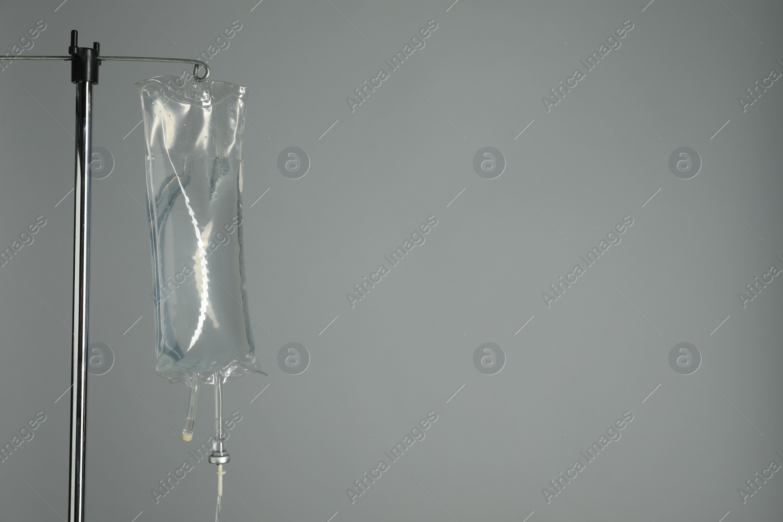 Photo of IV infusion set on pole against grey background. Space for text