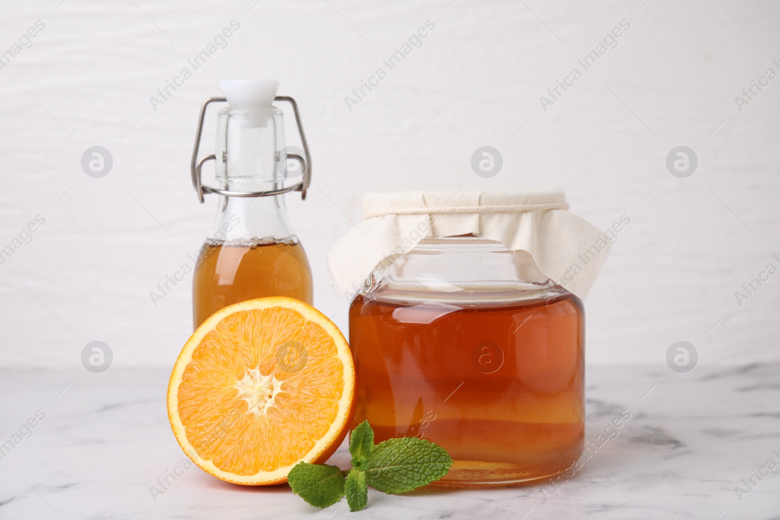 Photo of Tasty kombucha, orange and mint on white marble table