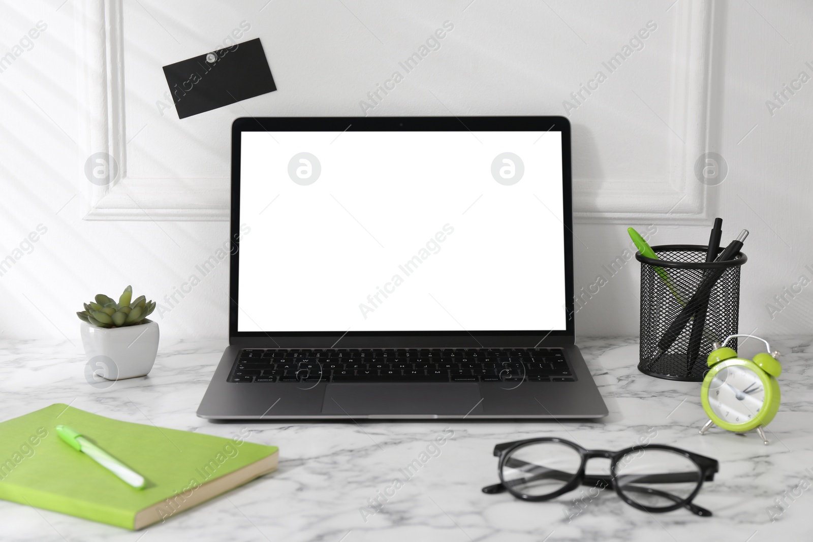 Photo of Office workplace with computer, glasses, houseplant and stationery on marble table near white wall