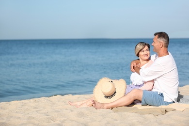 Happy mature couple sitting together at beach on sunny day