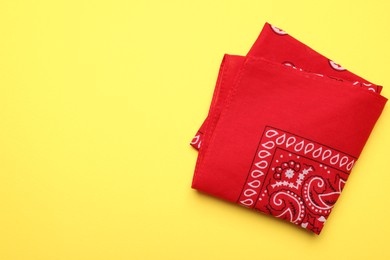 Photo of Folded red bandana with paisley pattern on yellow background, top view. Space for text