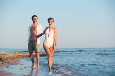 Happy young couple walking together on beach. Space for text