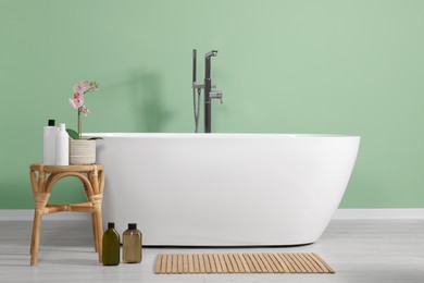 Stylish bathroom interior with ceramic tub, care products and beautiful orchid on coffee table