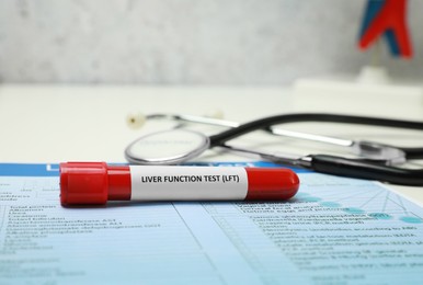 Liver Function Test. Tube with blood sample, form and stethoscope on table, closeup