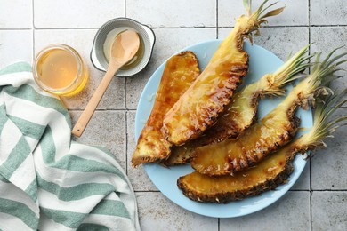 Photo of Tasty grilled pineapples, honey and wooden spoon on light gray tiled table, flat lay