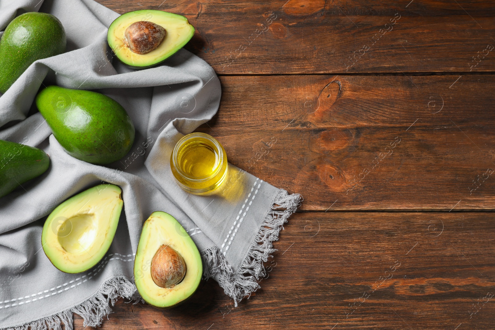 Photo of Jar with oil and ripe fresh avocados on wooden table, top view