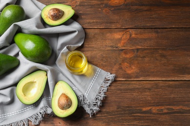 Photo of Jar with oil and ripe fresh avocados on wooden table, top view