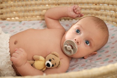 Cute little baby with pacifier and toy bear lying in cradle