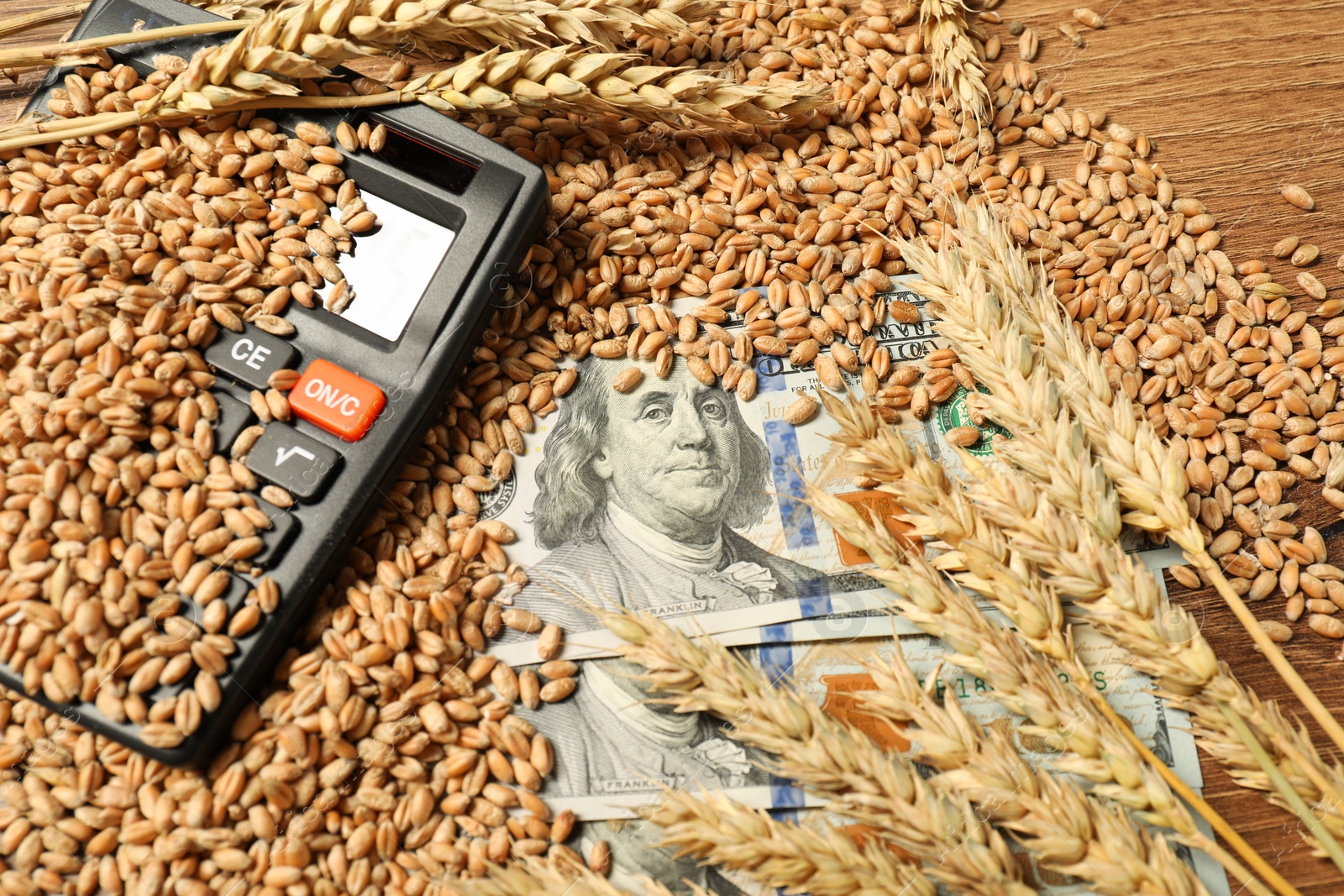 Photo of Wheat ears, grains, dollar banknotes and calculator on wooden table, closeup. Agricultural business