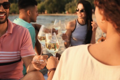 Photo of Group of friends having picnic outdoors at sunset, focus on glasses