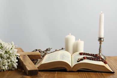 Church candles, cross, rosary beads, Bible, snowdrops and willow branches on wooden table against light background