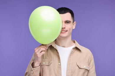 Photo of Happy young man with light green balloon on purple background