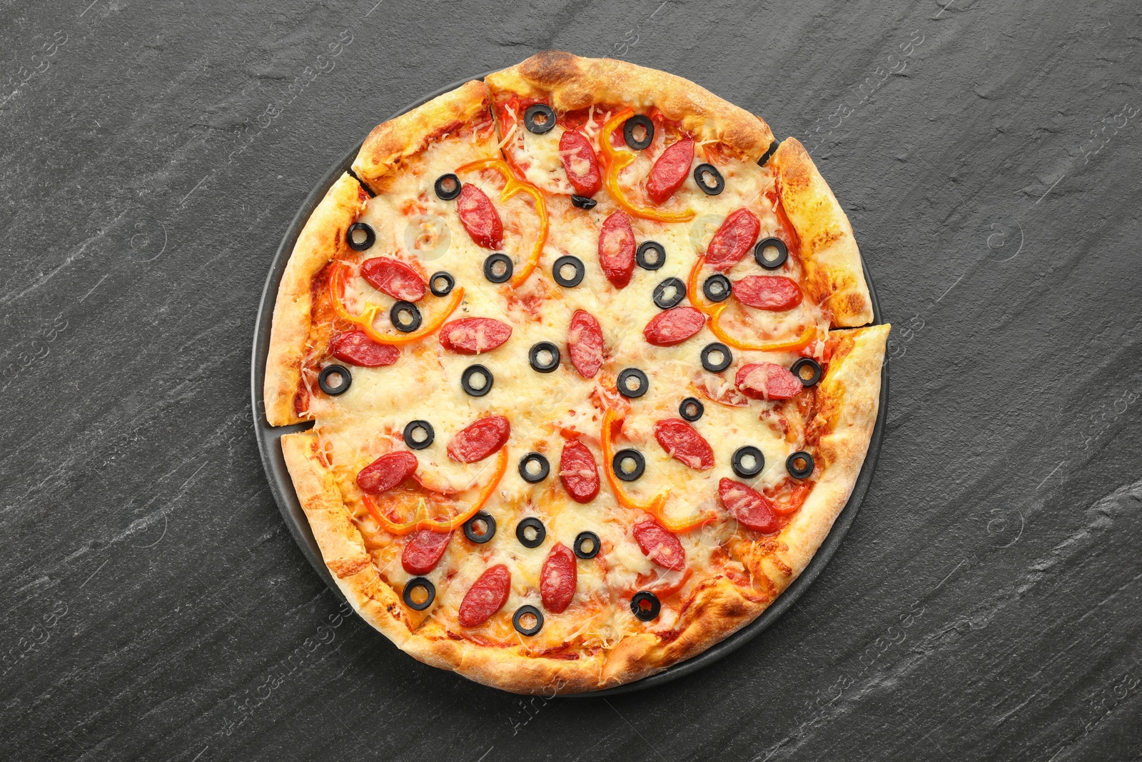 Photo of Tasty pizza with cheese, dry smoked sausages, olives and pepper on grey table, top view