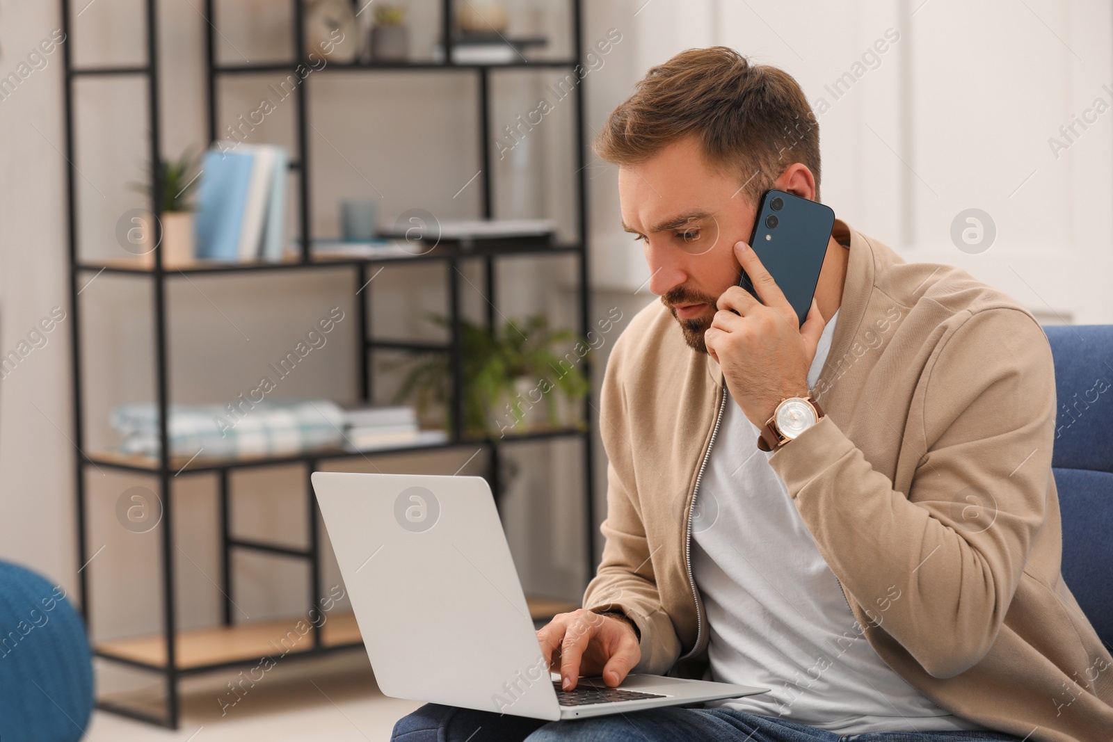 Photo of Young man talking on phone while working with laptop at home