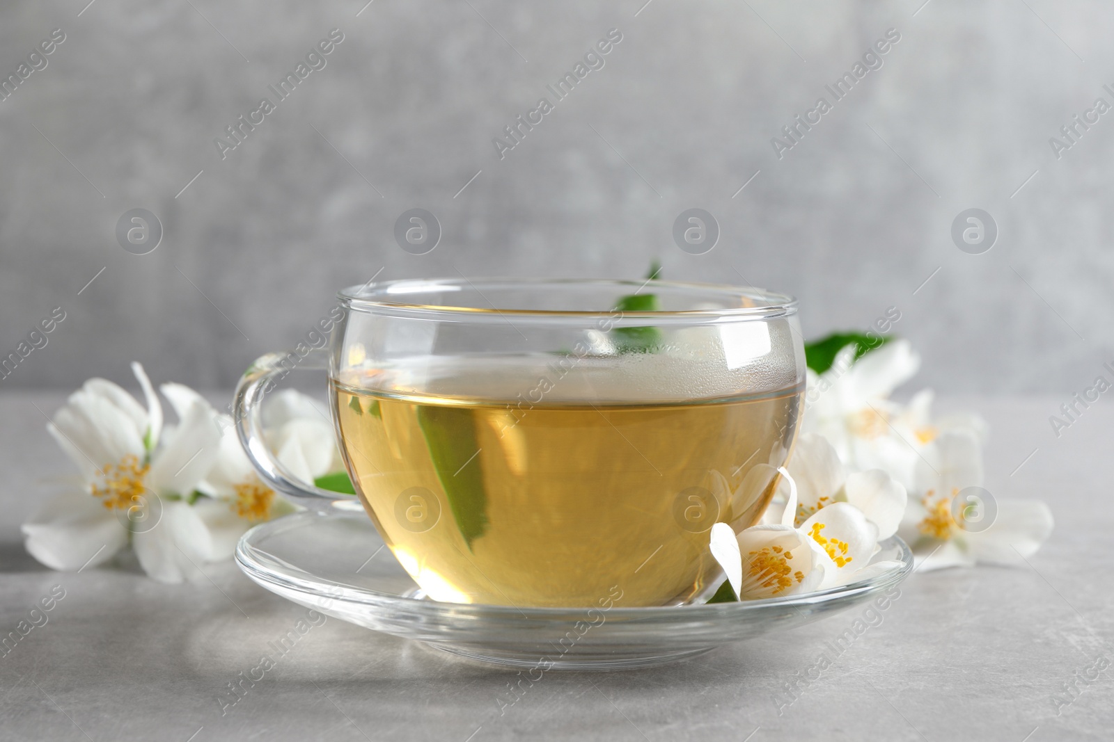 Photo of Glass cup of jasmine tea and fresh flowers on grey table