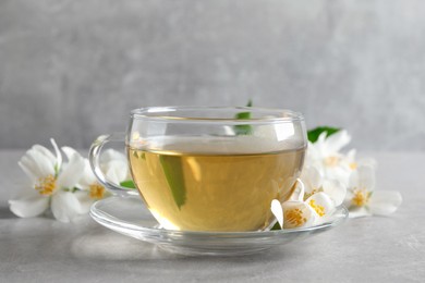 Glass cup of jasmine tea and fresh flowers on grey table