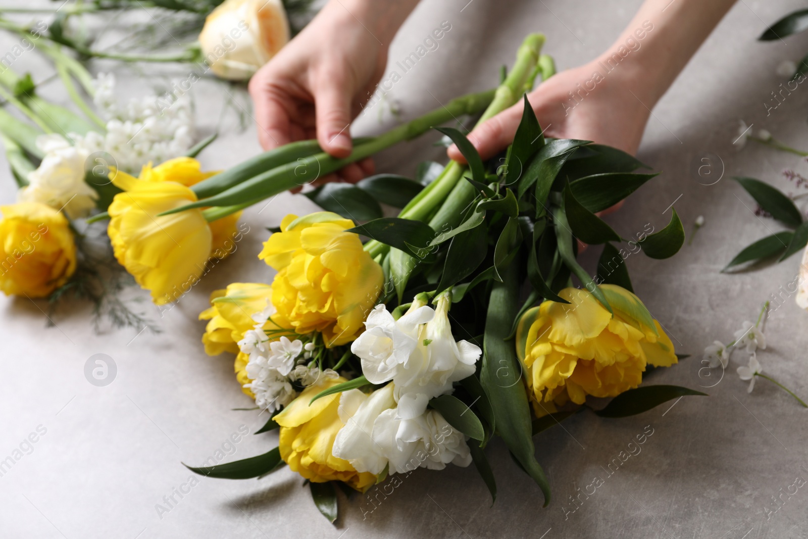 Photo of Florist making beautiful bouquet at grey table, closeup