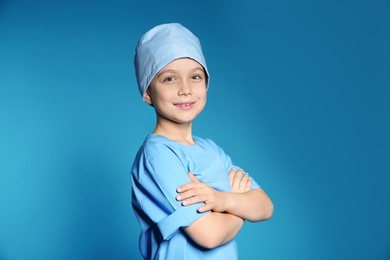 Photo of Cute little child in doctor uniform on color background