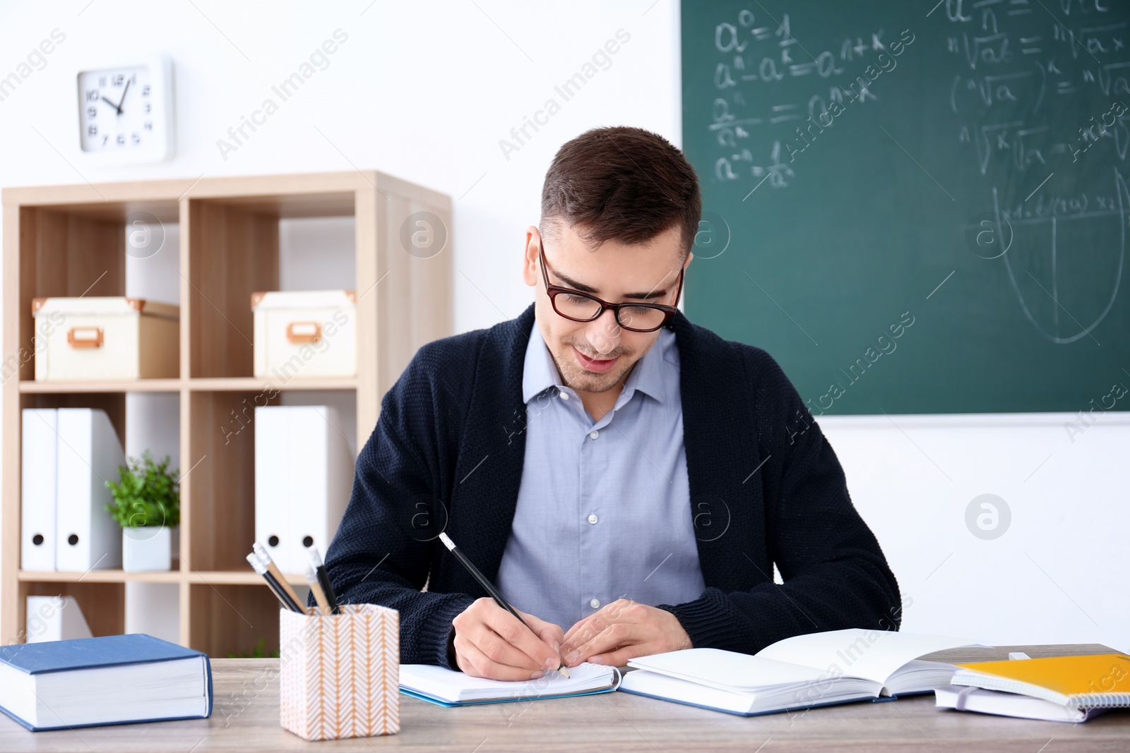 Photo of Young male teacher working at table in classroom