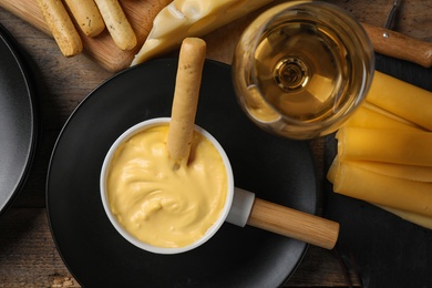 Flat lay composition with pot of tasty cheese fondue and products on wooden table