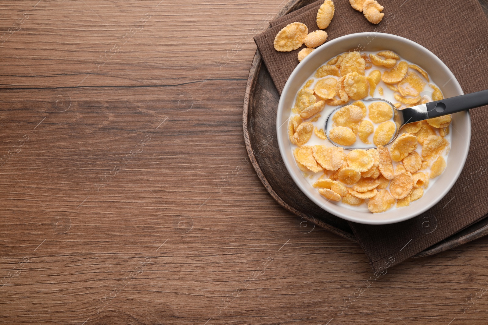 Photo of Tasty cornflakes with milk in bowl served on wooden table, top view. Space for text