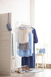 Photo of Wardrobe rack with women's clothes and different shoes at white brick wall in room