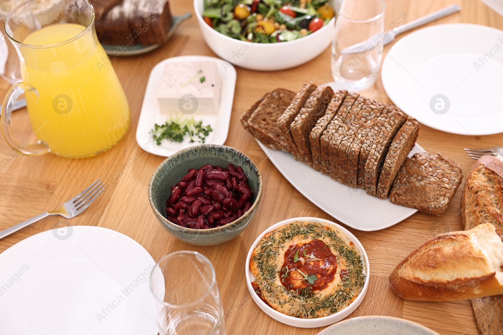 Photo of Healthy vegetarian food, jug of juice, glasses, cutlery and plates on wooden table