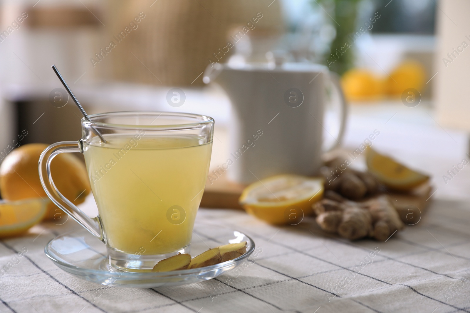 Photo of Glass of aromatic ginger tea and ingredients on white checkered tablecloth indoors, space for text