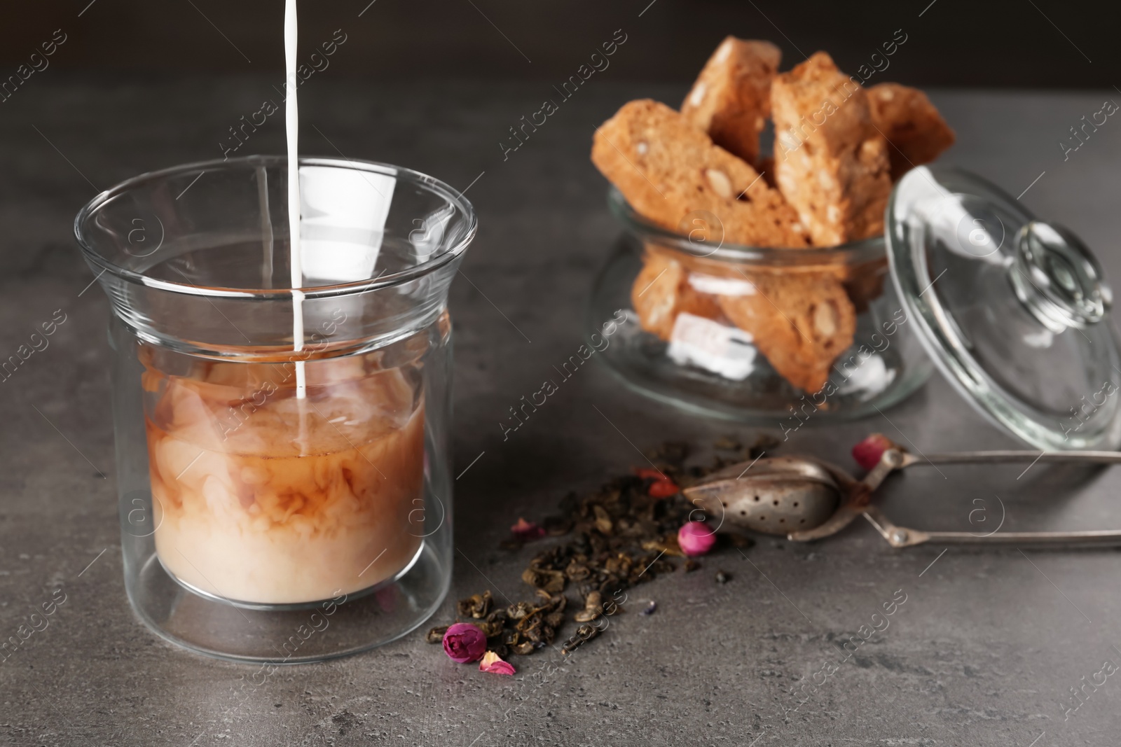 Photo of Adding milk to hot aromatic tea on grey table