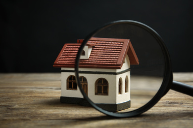 House model and magnifying glass on wooden table. Search concept