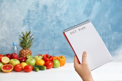 Photo of Woman holding notebook with words DIET PLAN near fruits on color background. Weight loss concept