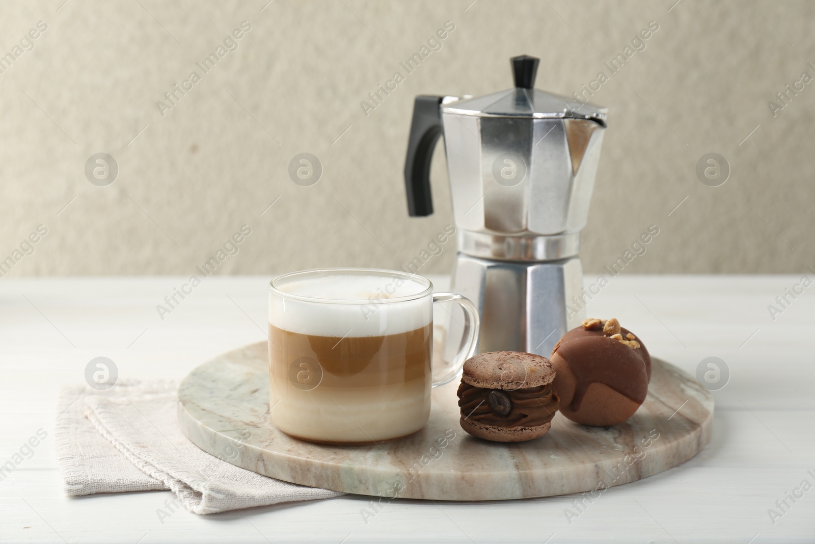 Photo of Aromatic coffee in cup, tasty macarons and moka pot on white wooden table