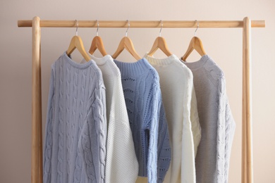 Photo of Collection of warm sweaters hanging on rack near light wall