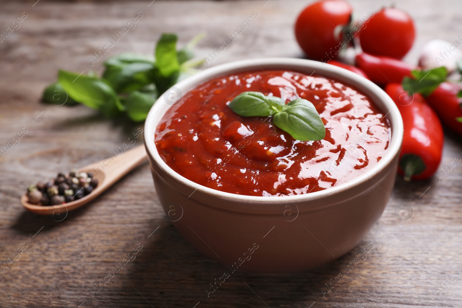 Photo of Bowl of spicy chili sauce on wooden table, closeup. Space for text