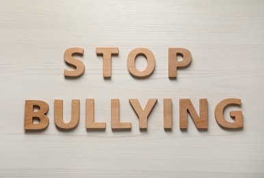 Photo of Text Stop Bullying of letters on white wooden table, flat lay