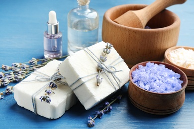 Photo of Handmade soap bars with lavender flowers and ingredients on blue wooden table, closeup