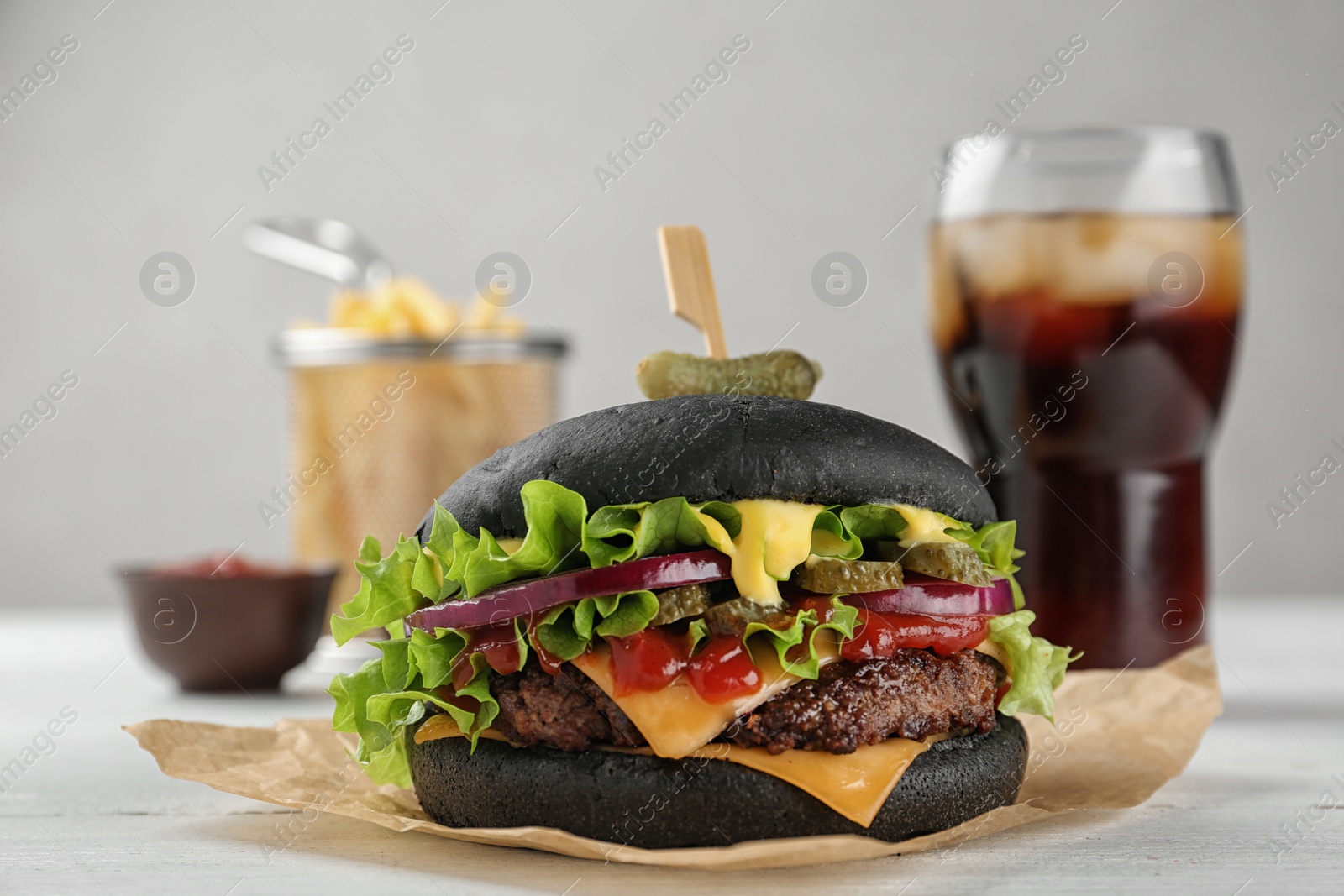 Photo of Tasty black burger served with French fries and cola on table