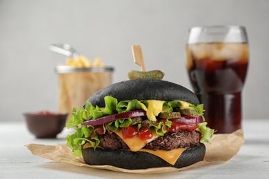 Photo of Tasty black burger served with French fries and cola on table