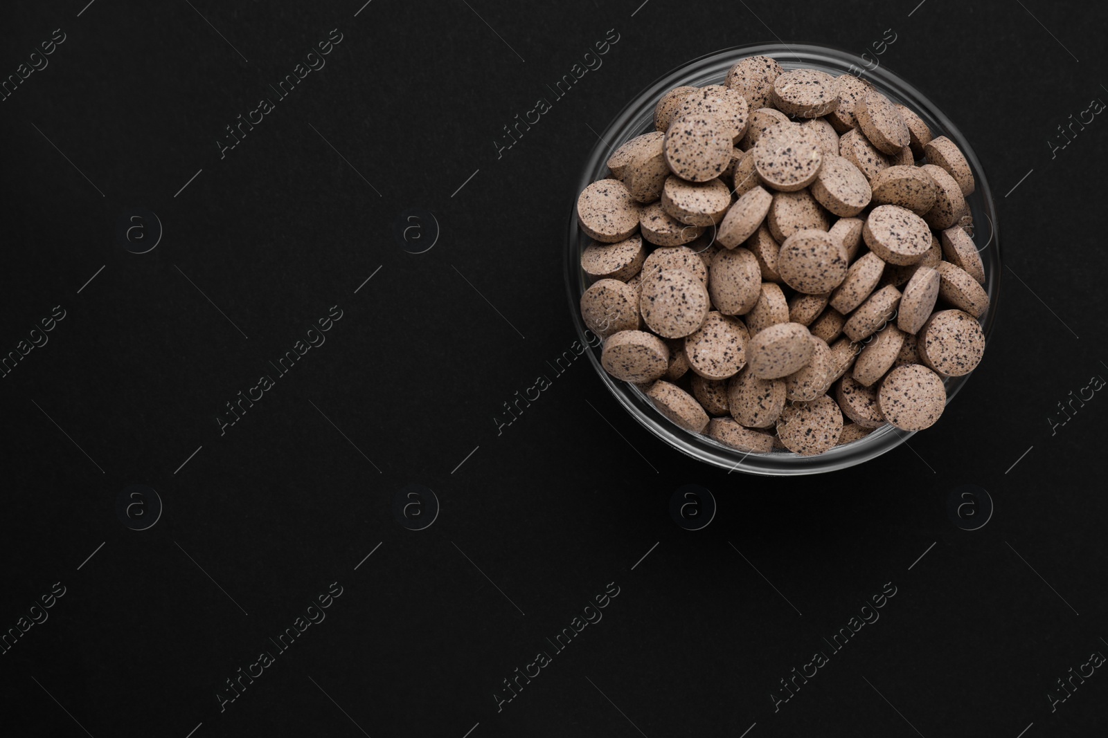 Photo of Glass bowl of brewer`s yeast tablets on black background, top view. Space for text