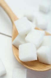 Many sugar cubes and wooden spoon on white table, closeup