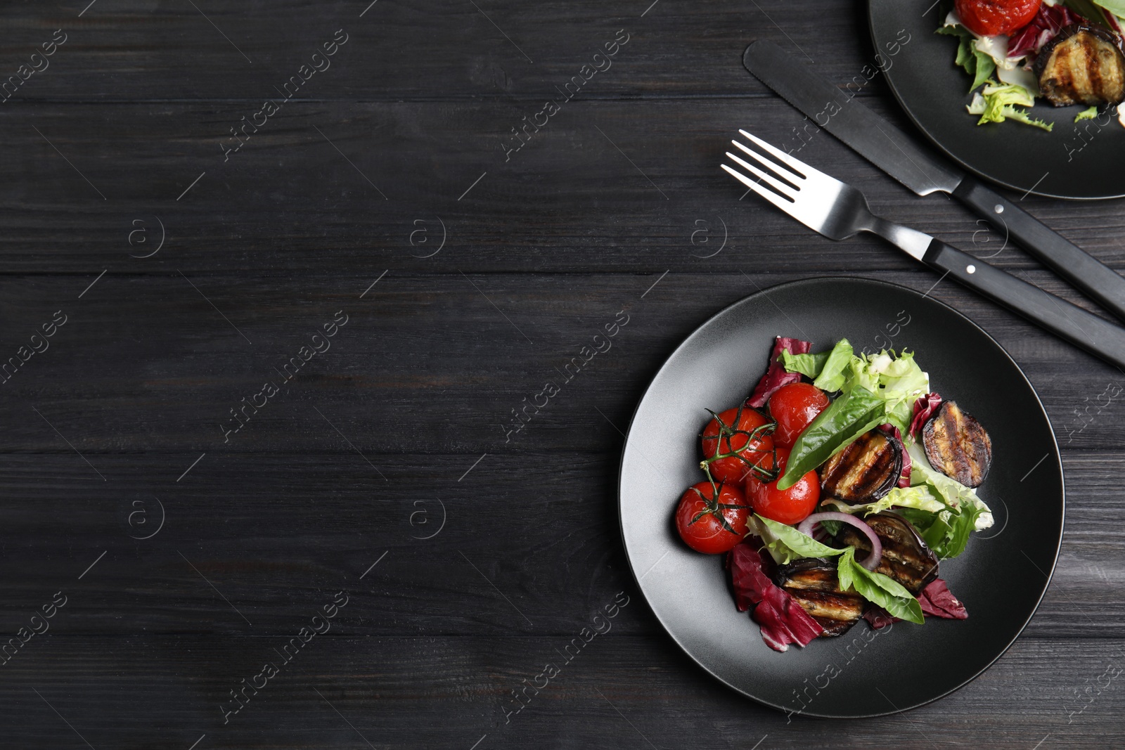 Photo of Delicious salad with roasted eggplant and basil served on black wooden table, flat lay. Space for text