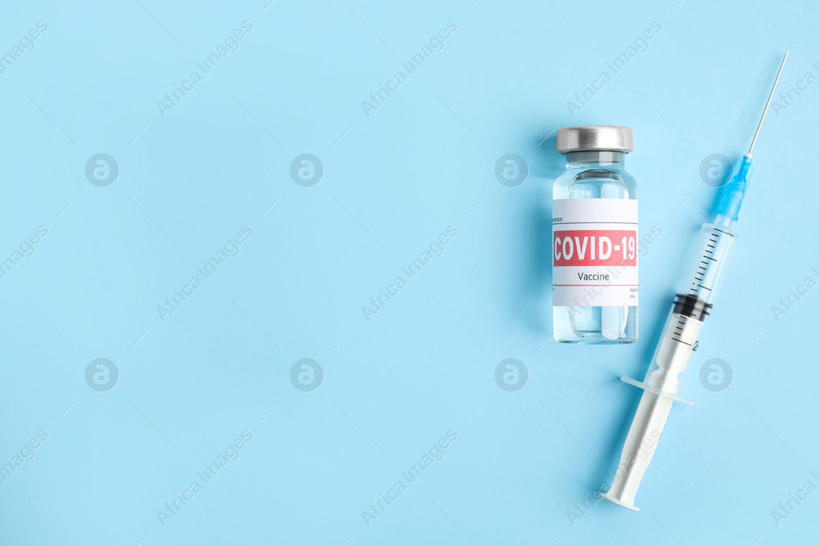 Photo of Vial with coronavirus vaccine and syringe on light blue background, flat lay. Space for text