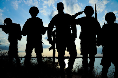 Image of Silhouettes of soldiers with assault rifles patrolling outdoors. Military service