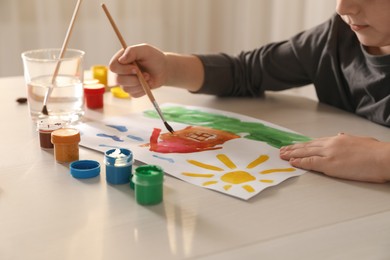Photo of Little boy drawing picture with brush at wooden table indoors, closeup. Child`s art
