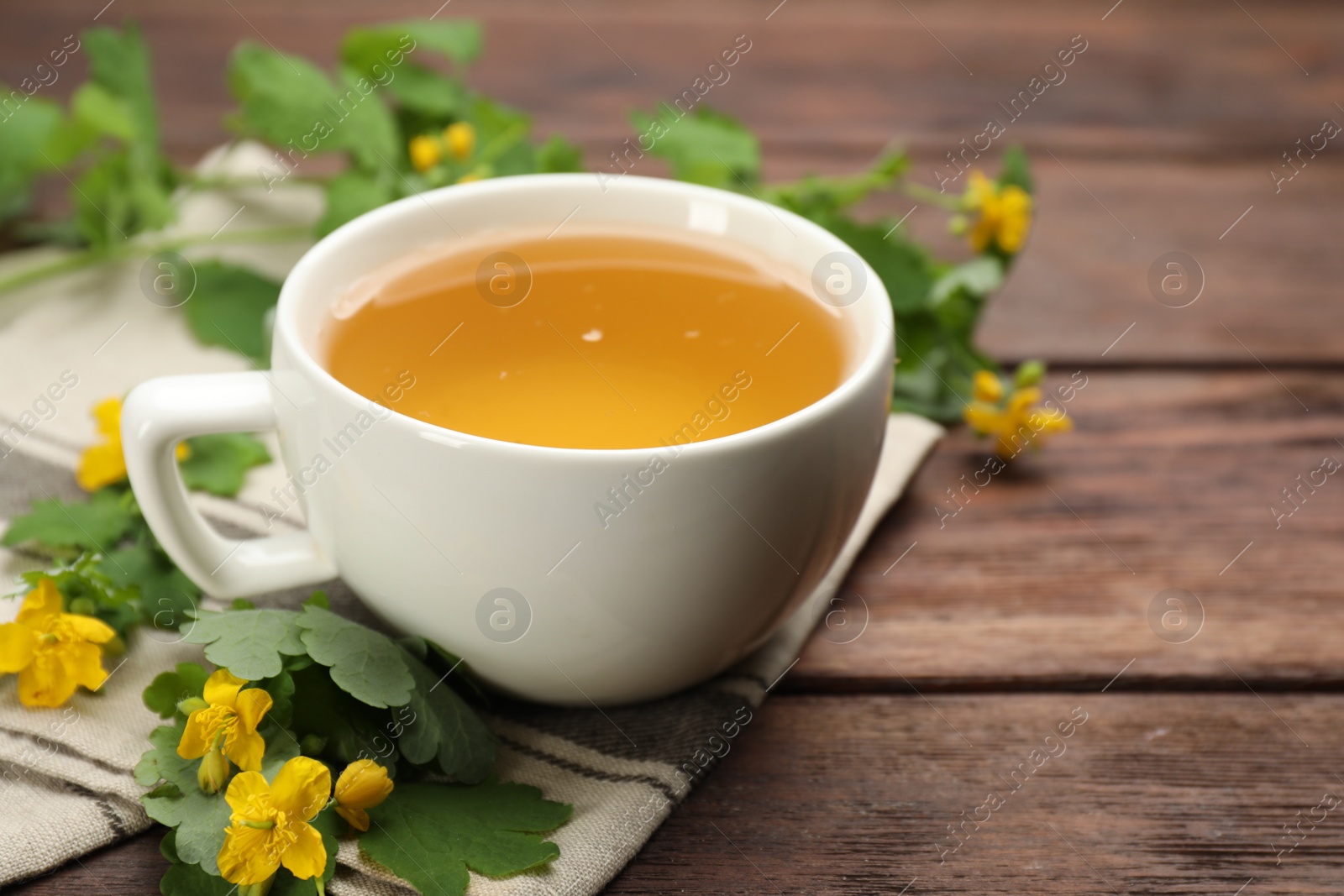 Photo of Cup of aromatic celandine tea and flowers on wooden table, closeup