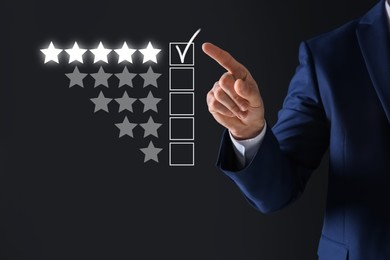 Image of Man choosing five stars on virtual screen against black background, closeup. Customer satisfaction score