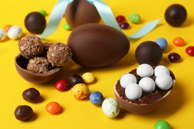 Tasty chocolate eggs and candies on yellow background