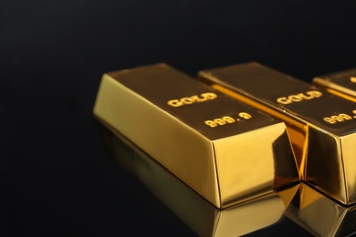 Photo of Shiny gold bars on black background, closeup. Space for text
